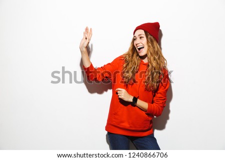 Portrait of a happy young woman wearing hoodie standing over white background, waving