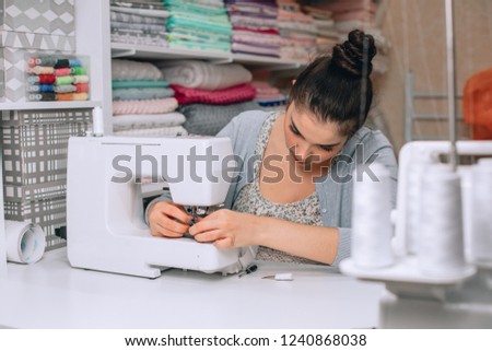 portrait of young woman seamstress sitting and sews on sewing machine. Tailor making a garment in her workplace. Hobby as a small business concept