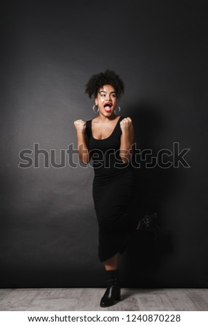 Full length photo of joyful afro american woman wearing black dress standing isolated over dark background