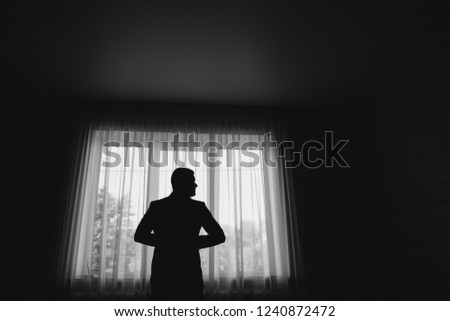 Man stand in front of window. Silhouette of young man. Black and white picture