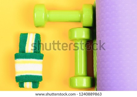 Workout and sport concept. Dumbbells made of light green plastic on yellow and purple yoga mat background, top view. Shaping and fitness equipment. Barbells with white and green hand band