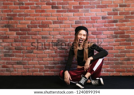 Photo of beautiful young hip hop dancer or sporty girl sitting on floor against brick wall