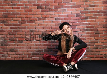 Photo of teenage hip hop dancer or sporty woman sitting on floor against brick wall