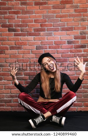 Photo of trendy hip hop dancer or sporty woman sitting on floor against brick wall
