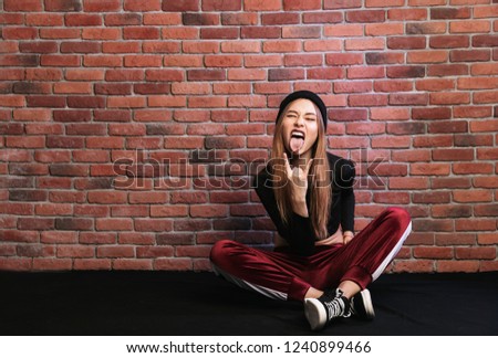 Photo of stylish hip hop dancer or sporty girl sitting on floor against brick wall