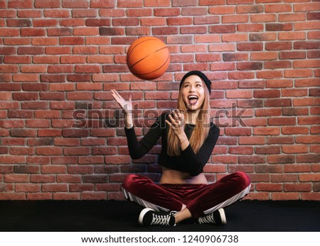 Photo of teen sporty woman 20s sitting on floor against brick wall and playing with basketball