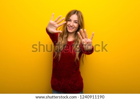 Young girl on vibrant yellow background counting nine with fingers