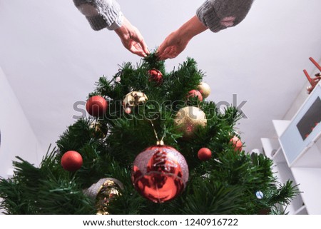Bottom view of young woman in sweater decorating Christmas tree with balls. New Year and Christmas time. Holidays concept.
