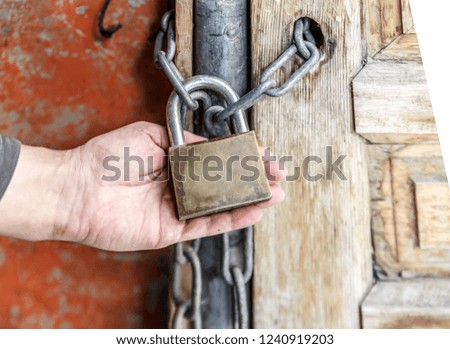 A hand holds a padlock that keeps a wooden door closed