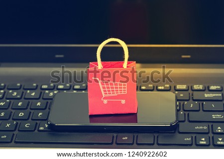 Ecommerce concept. : Red paper shopping bags with smartphone on notebook keyboard. International freight or shipping service for online shopping Royalty-Free Stock Photo #1240922602