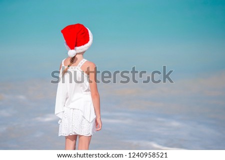 Back view of little girl in red Santa hat on tropical beach on Christmas vacation