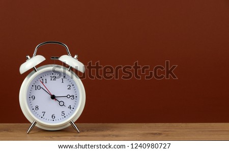 white classic style alarm clock on wooden table - 4:15 o'clock