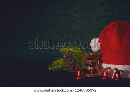 Red Santa hat and Xmas bells with fir branches and fir cones on dark blurred background