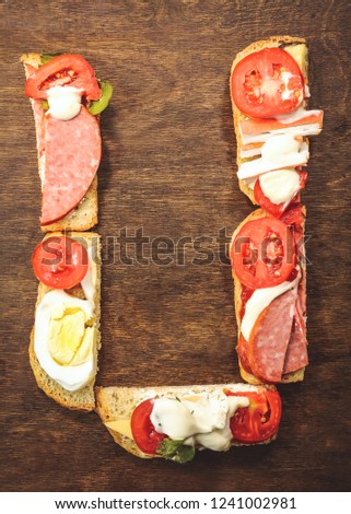 alphabet letter - U, from sandwiches with sausage, tomatoes and egg.  on dark wooden background