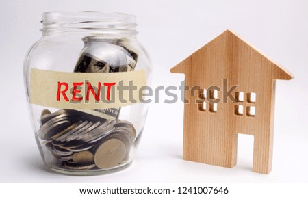 Glass jar with the words Rent and a wooden house. The concept of saving money for rental housing. Accumulation money for an apartment. Rental payment. Renting a home. Real estate