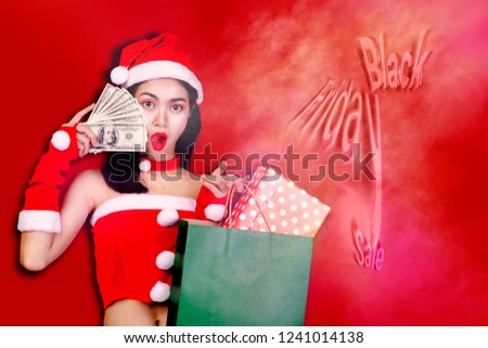Beautiful young woman make shopping in black friday holiday. Girl with red Santa Claus,many Dollars notes in hand, alpha kid has hold gift boxes in many  bags, on red background design, New year sale