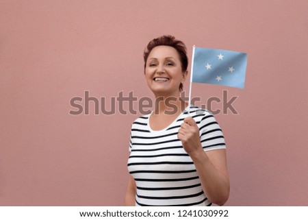 Micronesia flag. Woman holding Micronesia flag. Nice portrait of middle aged lady 40 50 years old with a national flag over pink wall background outdoors.