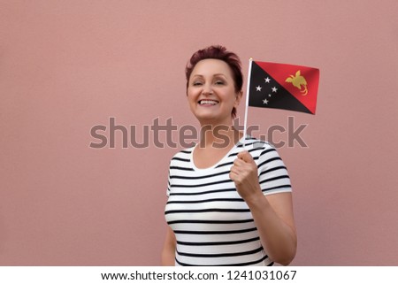 Papua New Guinea flag. Woman holding Papua New Guinea flag. Nice portrait of middle aged lady 40 50 years old with a national flag over pink wall background outdoors.