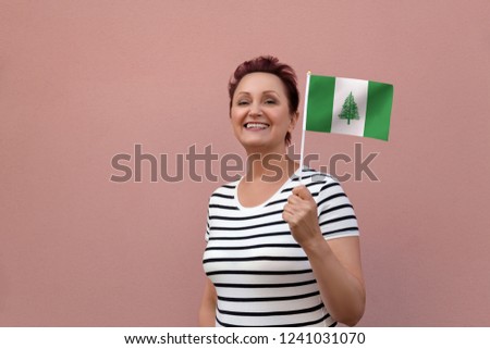 Norfolk Island flag. Woman holding Norfolk Island flag. Nice portrait of middle aged lady 40 50 years old with a national flag over pink wall background outdoors.