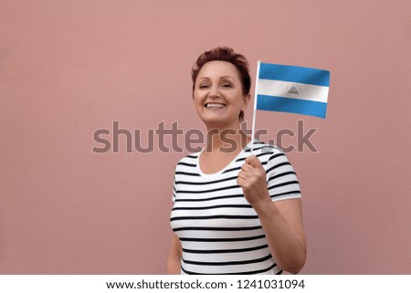 Nicaragua flag. Woman holding Nicaragua flag. Nice portrait of middle aged lady 40 50 years old with a national flag over pink wall background outdoors.