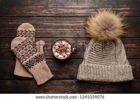 Winter flat lay with mitten, knitted hat and mug with hot chocolate or cocoa with marshmallow on dark rustic wooden table. Christmas and new year background. Top view