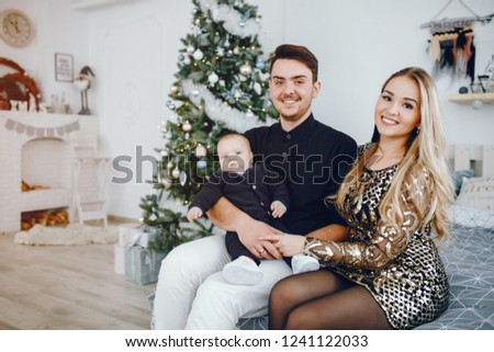 Beautiful family sitting on a bed near Christmas tree. Cute mother in a elegants dress.