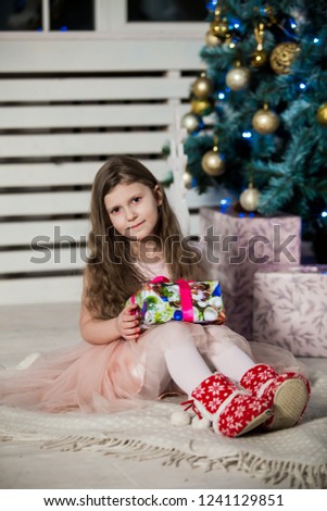 Little girl with Christmas gifts  in hand near a Christmas tree at home. New Year. Christmas eve. Holiday.