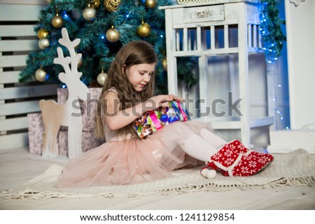 Little girl with Christmas gifts  in hand near a Christmas tree at home. New Year. Christmas eve. Holiday.