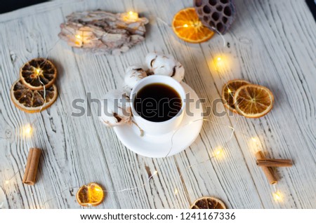 A cup of coffee with cotton and oranges on a wooden background.