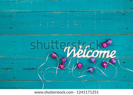 Welcome sign with Christmas ornaments and white ribbon on teal blue rustic wood background; holiday background with copy space