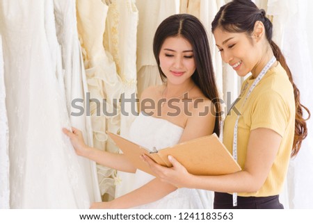 Female dressmaker helping the customer choosing the wedding dress design from catalog.