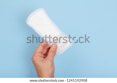 White sanitary pad in the woman's hand on a blue background. Absorbent item for women special days. Hygiene and health concept.