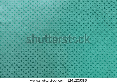 Dark turquoise background from metal foil paper with a pattern of sparkling stars closeup. Texture of cyan metallized wrapping holiday paper surface.