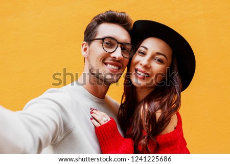  Close up lifestyle photo of Happy girl with her boyfriend making self portrait by mobile phone. Yellow background.  Wearing red knitted sweater. New year party mood.