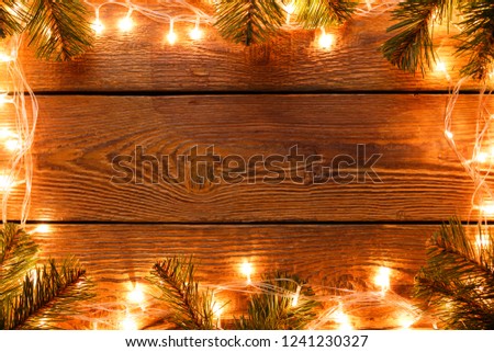 Image of wooden surface with burning garland around perimeter, branches of spruce.