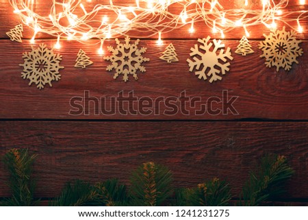 Photo of New Year's wooden red table with burning garland on top, snowflakes, spruce branches.