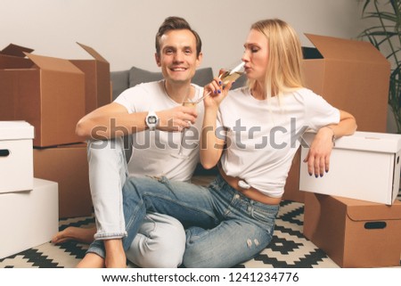 Image of smiling couple with champagne glasses sitting among cardboard boxes