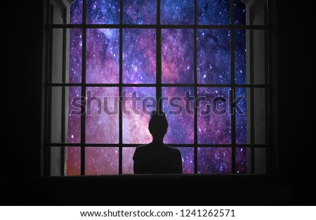 Silhouette of a girl looking a dreamlike galaxy through a window. Fantasy picture.