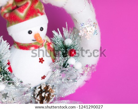 Christmas background of pretty snowman doll in white soft christmas wreath on pink background with copy space.