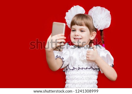 Cute little girl in white bows hold telephone and take picture on red background. Communication concept