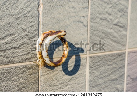 Hook, rusted metal safety hook in front of shop with tiled facade, selective focus