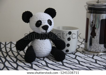 Knitted panda sitting on table near coffee cup