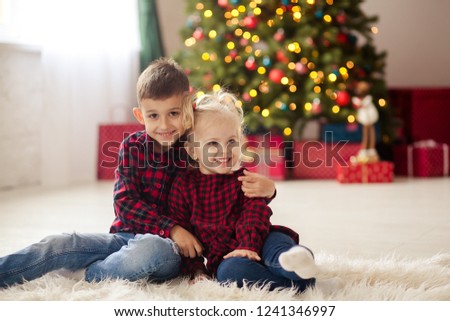 happy cute brother and sister at the Christmas tree, red stylish shirts and jeans, children hug and rejoice in the new year