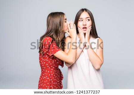 Two excited young girls dressed in summer clothes whispering secrets isolated over white background