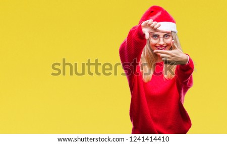 Young beautiful blonde woman wearing christmas hat over isolated background smiling making frame with hands and fingers with happy face. Creativity and photography concept.