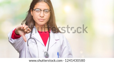 Young arab doctor woman over isolated background looking unhappy and angry showing rejection and negative with thumbs down gesture. Bad expression.
