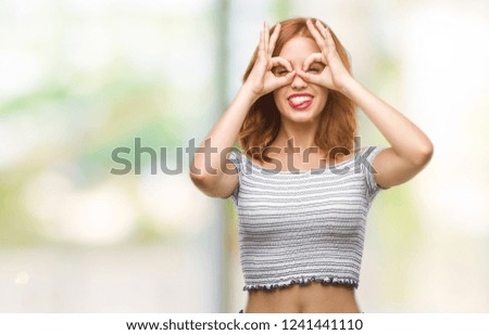 Young beautiful woman over isolated background doing ok gesture like binoculars sticking tongue out, eyes looking through fingers. Crazy expression.