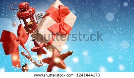 Christmas present with ornaments falling over blue background covered by snowflakes with empty space