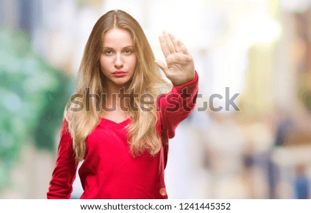 Young beautiful blonde woman wearing red sweater over isolated background doing stop sing with palm of the hand. Warning expression with negative and serious gesture on the face.