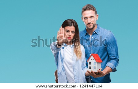 Young couple in love holding house over isolated background with open hand doing stop sign with serious and confident expression, defense gesture